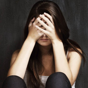 A studio shot of a sad young woman holding her head in her hands